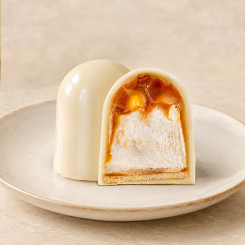 White chocolate flødebolle with salted caramel filling on a biscuit base, one whole and one cut in half